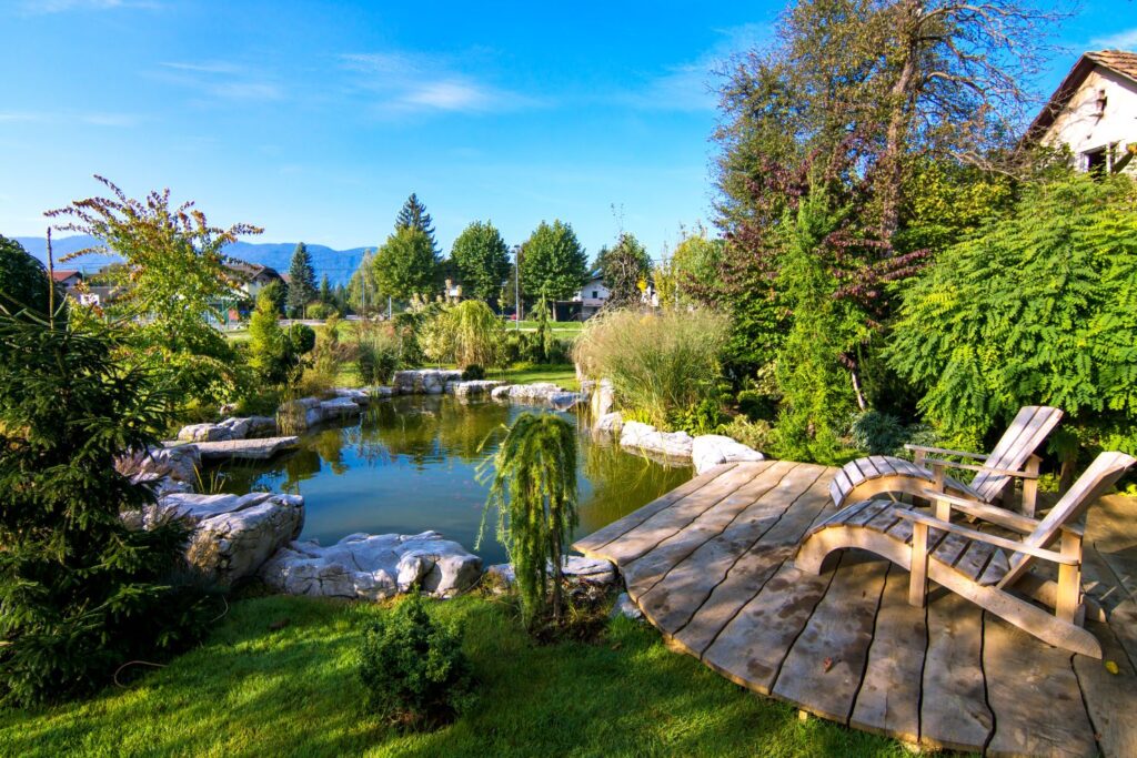 A pond installed in a backyard, with a deck that has two wooden chaise lounges.