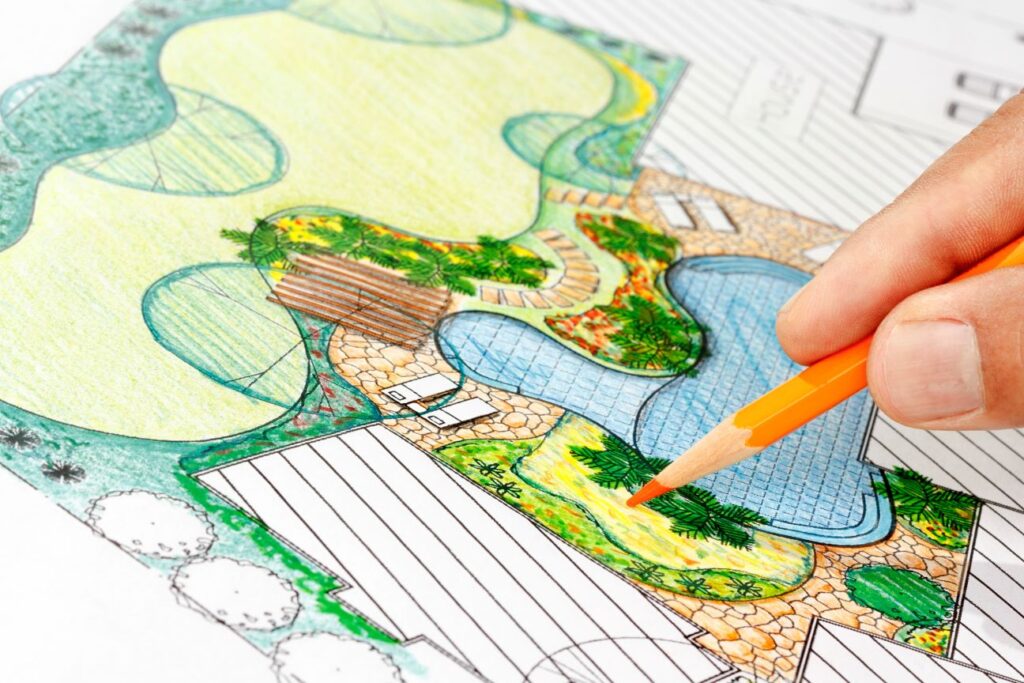 A hand holds a pencil over a detailed drawing of a landscape design.